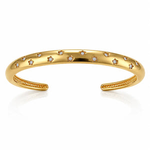 A polished gold open cuff bracelet decorated with small star-shaped settings holding clear round stones, shown on a clean white background with a soft reflection below.