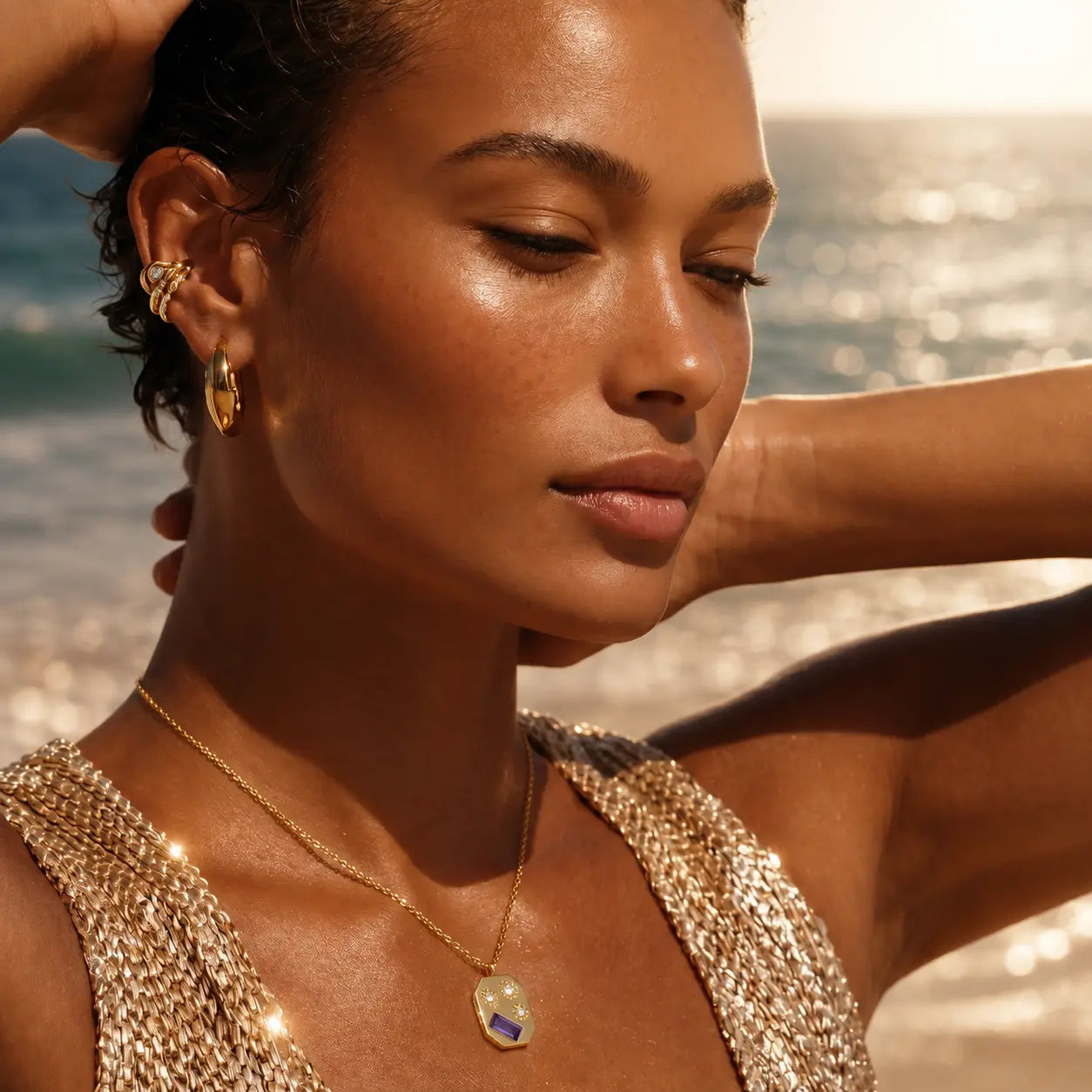 Woman on a beach wearing gold jewelry with a blurred ocean background