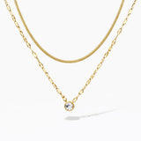Layered gold necklaces with a solitaire crystal pendant on a white background