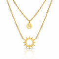 A double-layered gold necklace set featuring a delicate cable chain with a small smiley face disc pendant and a thicker link chain with a sunburst pendant, displayed on a clean white background with a soft reflection.
