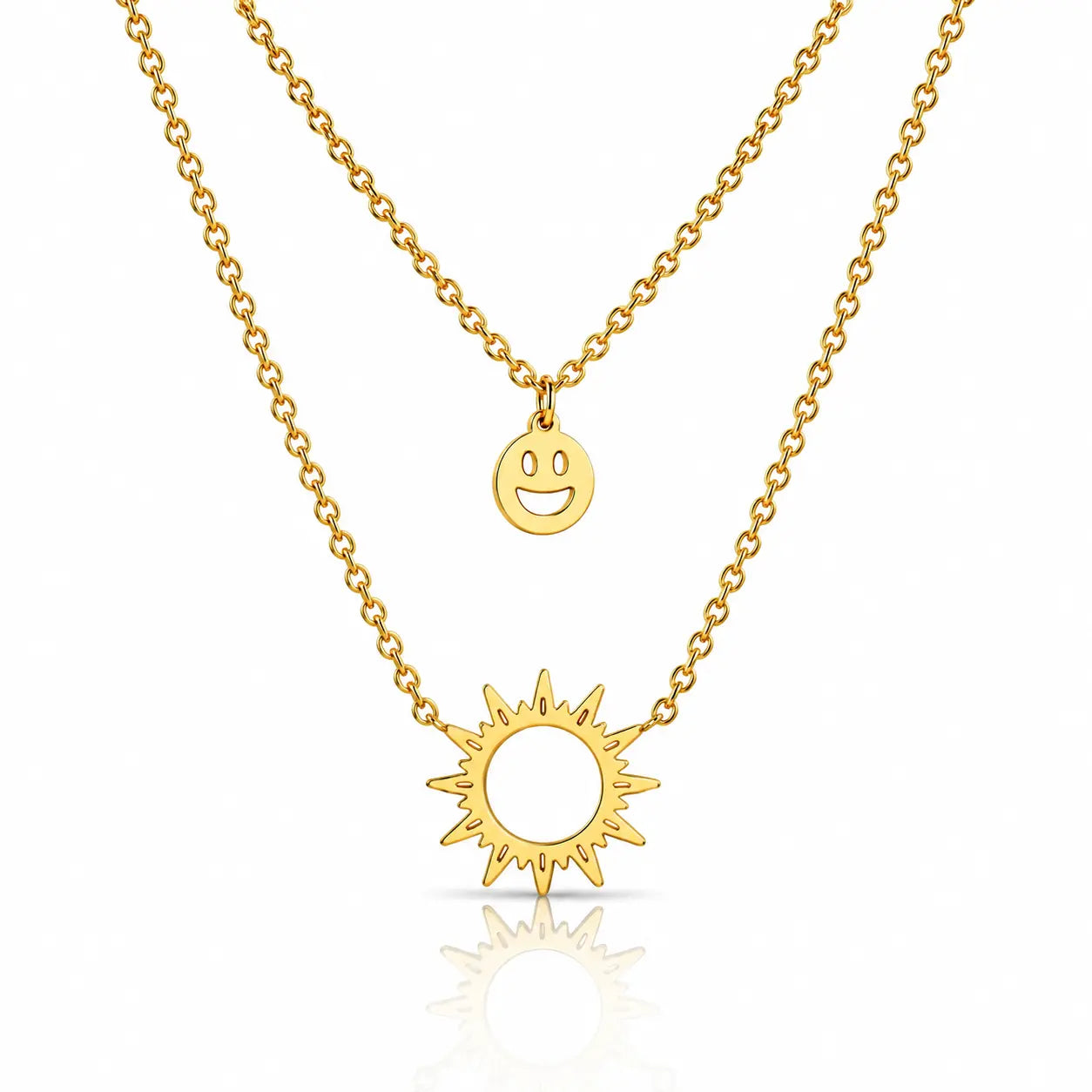 A double-layered gold necklace set featuring a delicate cable chain with a small smiley face disc pendant and a thicker link chain with a sunburst pendant, displayed on a clean white background with a soft reflection.