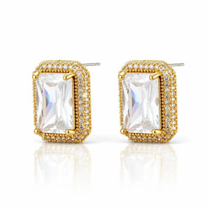 A pair of gold-plated rectangular stud earrings featuring a large clear emerald-cut center stone surrounded by a halo of small clear stones, set against a clean white background with a soft reflection.