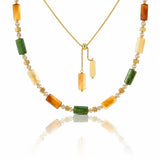 A gold necklace featuring rectangular green and amber-orange stone beads separated by small gold floral spacers, displayed on a clean white background with a soft reflection below.