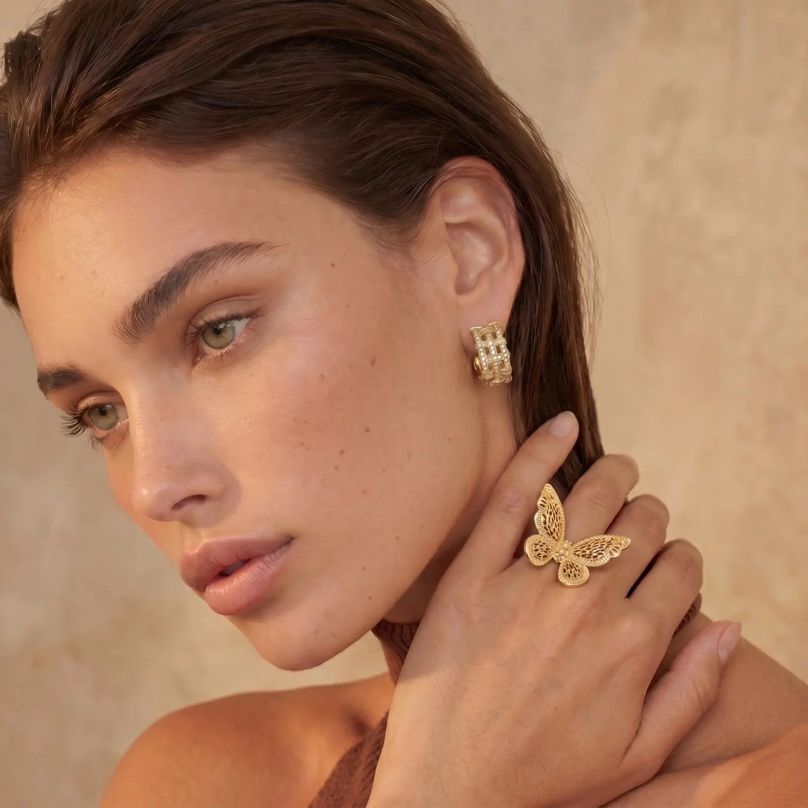 Woman wearing gold butterfly earrings and ring against a beige background