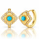 A pair of gold hoop earrings with a matching square flower-shaped front piece, featuring turquoise blue center stones surrounded by clear cubic zirconia accents, shown on a white background with a soft reflection.