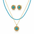 A gold and turquoise jewelry set featuring a double-strand beaded necklace with a round pendant, matching stud earrings, and a gold chain with a round pendant, all displayed on a clean white background.