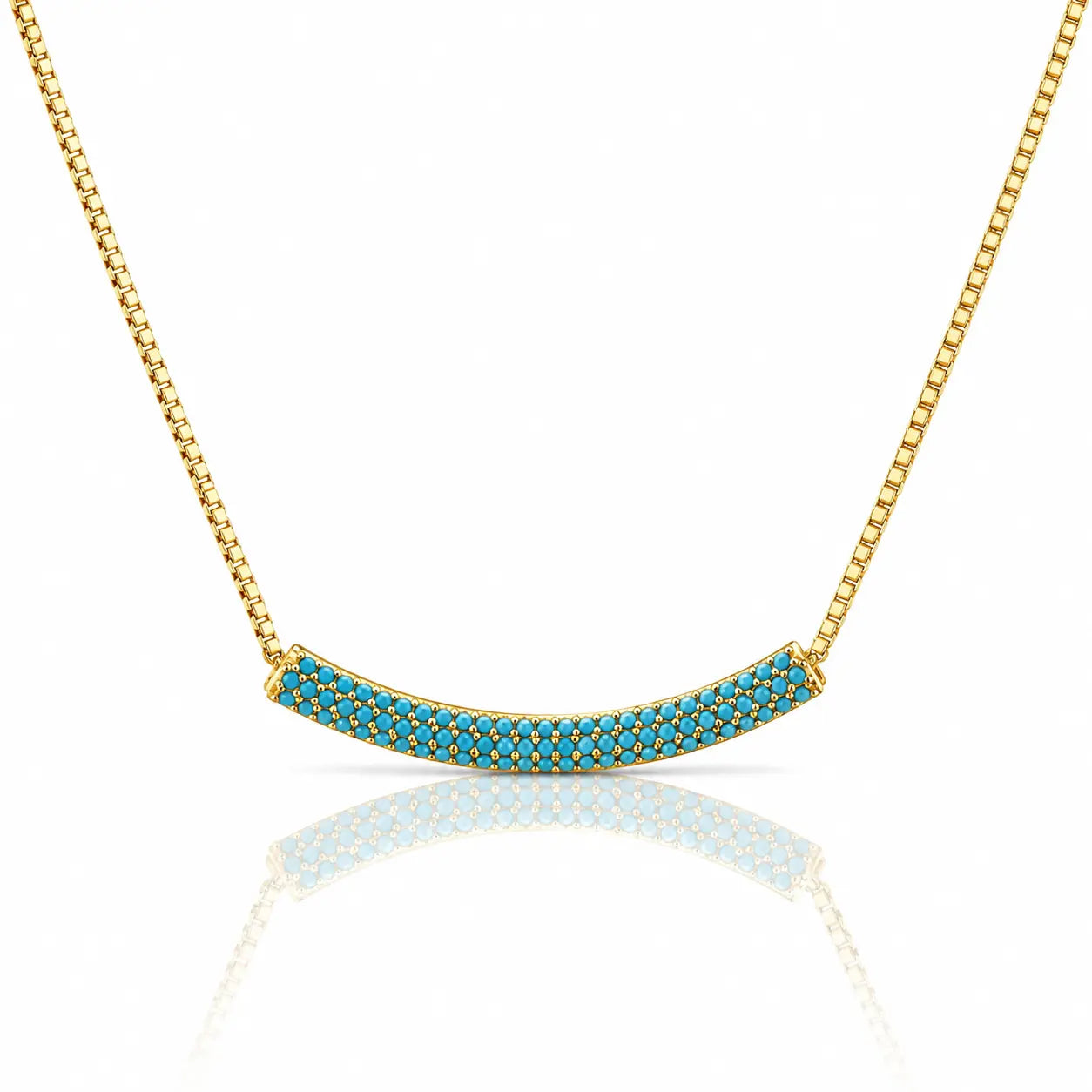 Gold necklace with a curved bar pendant paved with small turquoise-blue stones, shown on a white background with a soft reflection below.