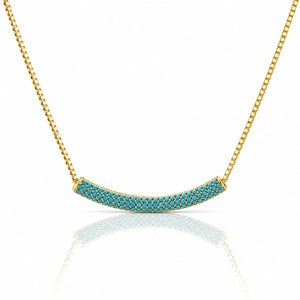 Gold necklace with a curved bar pendant paved with small turquoise-blue stones, shown on a white background with a soft reflection below.
