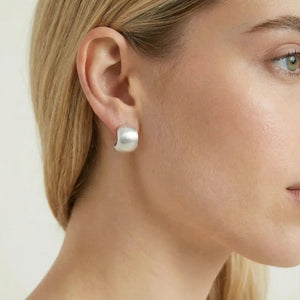 Woman wearing minimalist curved silver stud earring on ear, close-up jewelry photo