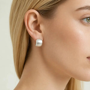A close-up of a woman's ear wearing a single small, polished silver stud earring with a rounded, polished stone.