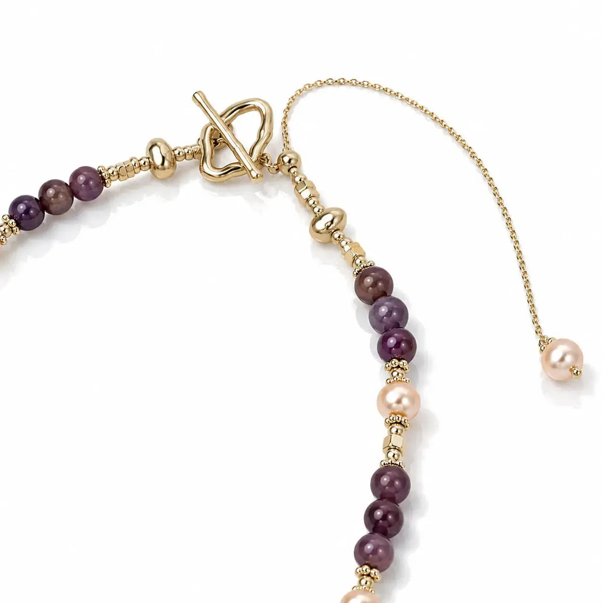 A close-up of a delicate gold-tone beaded necklace featuring alternating strands of deep purple beads and pale pink freshwater pearls, with a toggle clasp and extender chain on a white background.