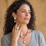 Woman wearing jewelry including a necklace, ring, and earrings against a beige background