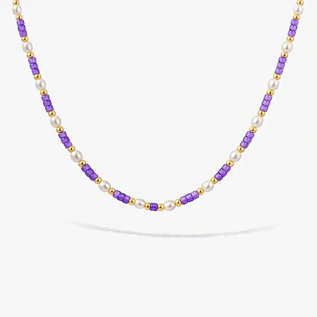 Pearl and gold beaded necklace with violet cube beads on white background