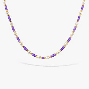 Pearl and gold beaded necklace with violet cube beads on white background