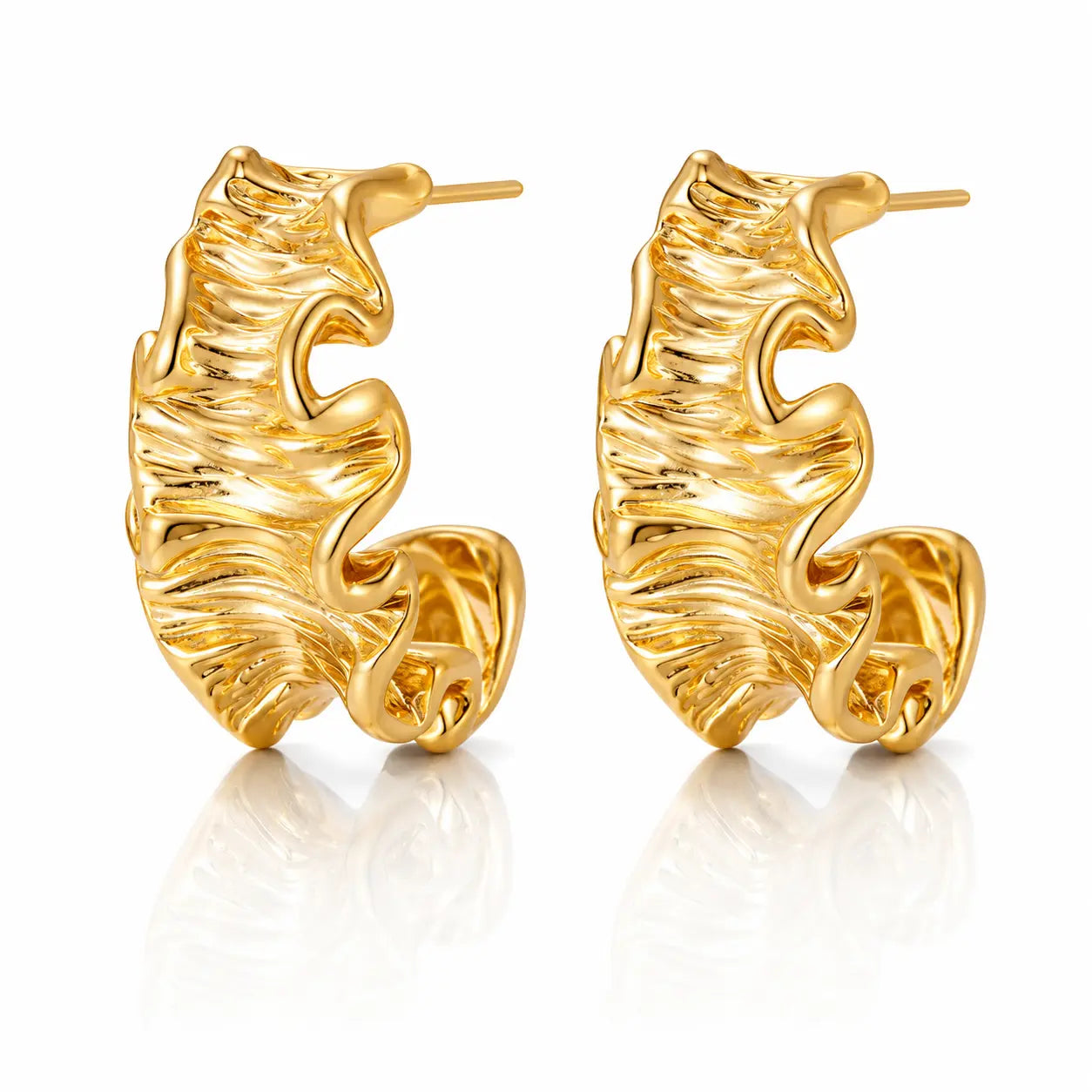 A pair of gold huggie hoop earrings with a textured, organic wavy surface, displayed on a clean white background with a soft reflection below.