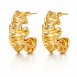 A pair of gold huggie hoop earrings with a textured, organic wavy surface, displayed on a clean white background with a soft reflection below.