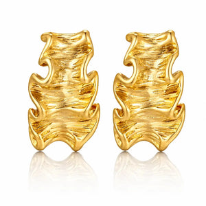 A pair of textured gold huggie hoop earrings with a wavy, organic flame-like design, displayed on a clean white background with a soft reflection below.