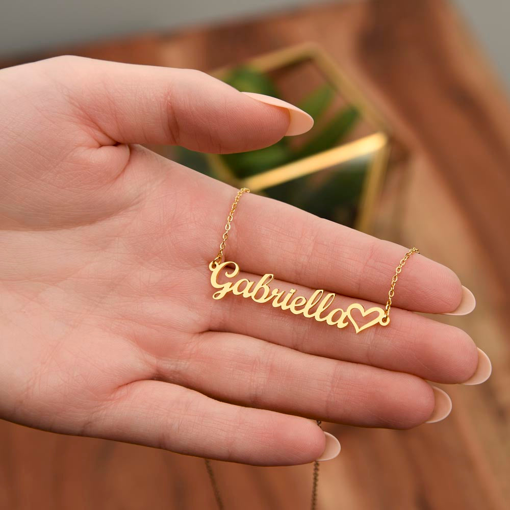 Close-up of custom name necklace with heart detail held in hand