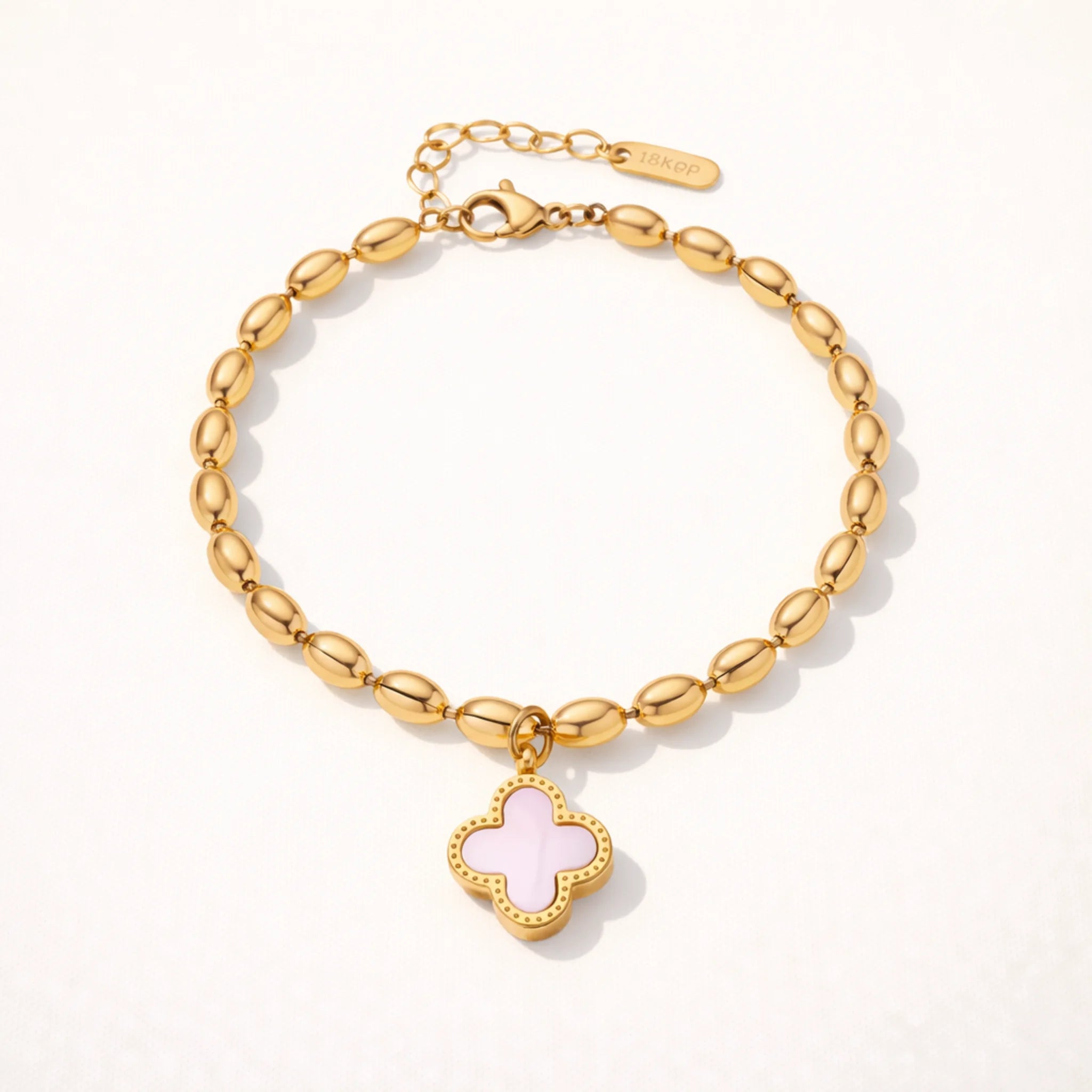 Gold bracelet with a pink clover charm on a white background
