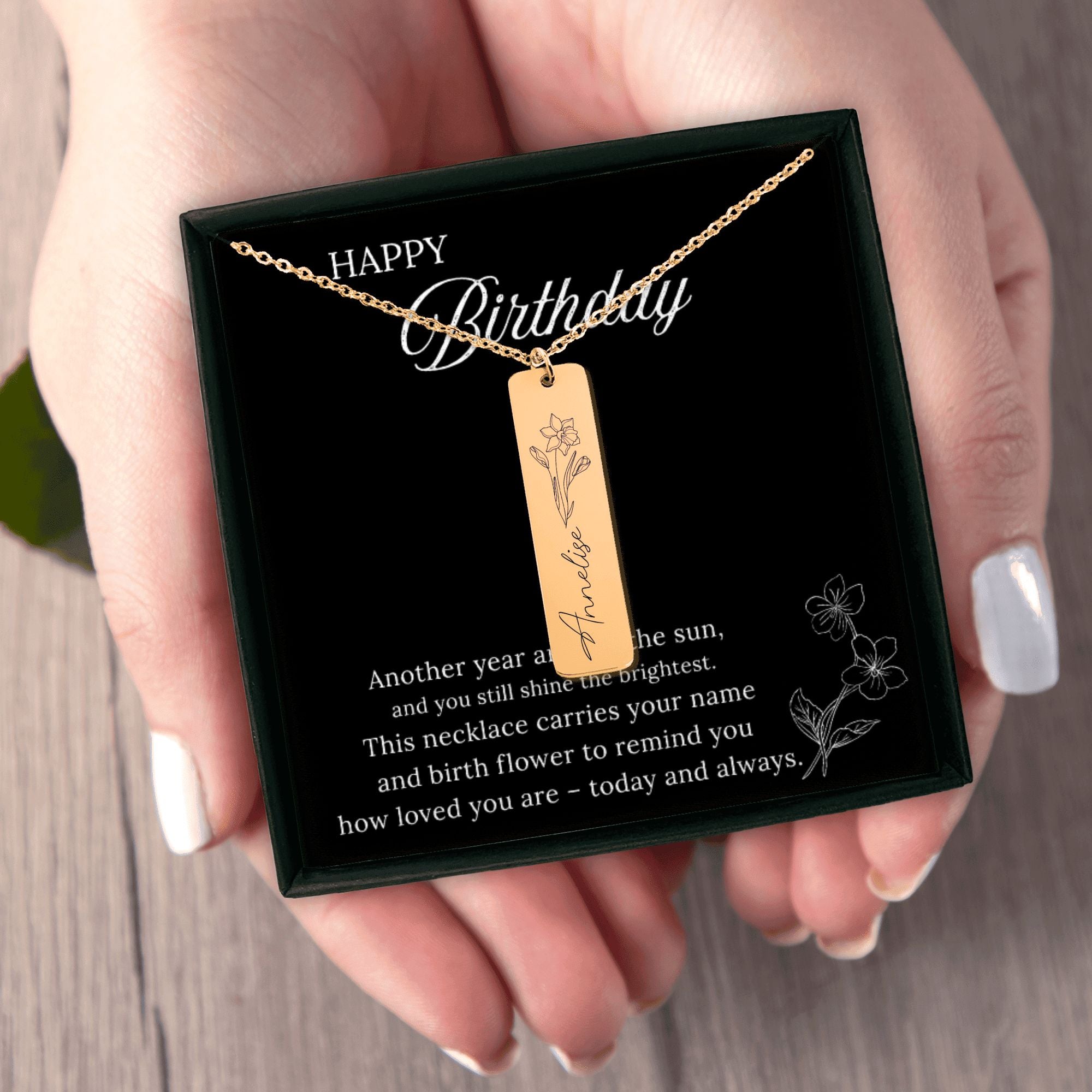 Gold necklace with a pendant on a 'Happy Birthday' card held by a hand.
