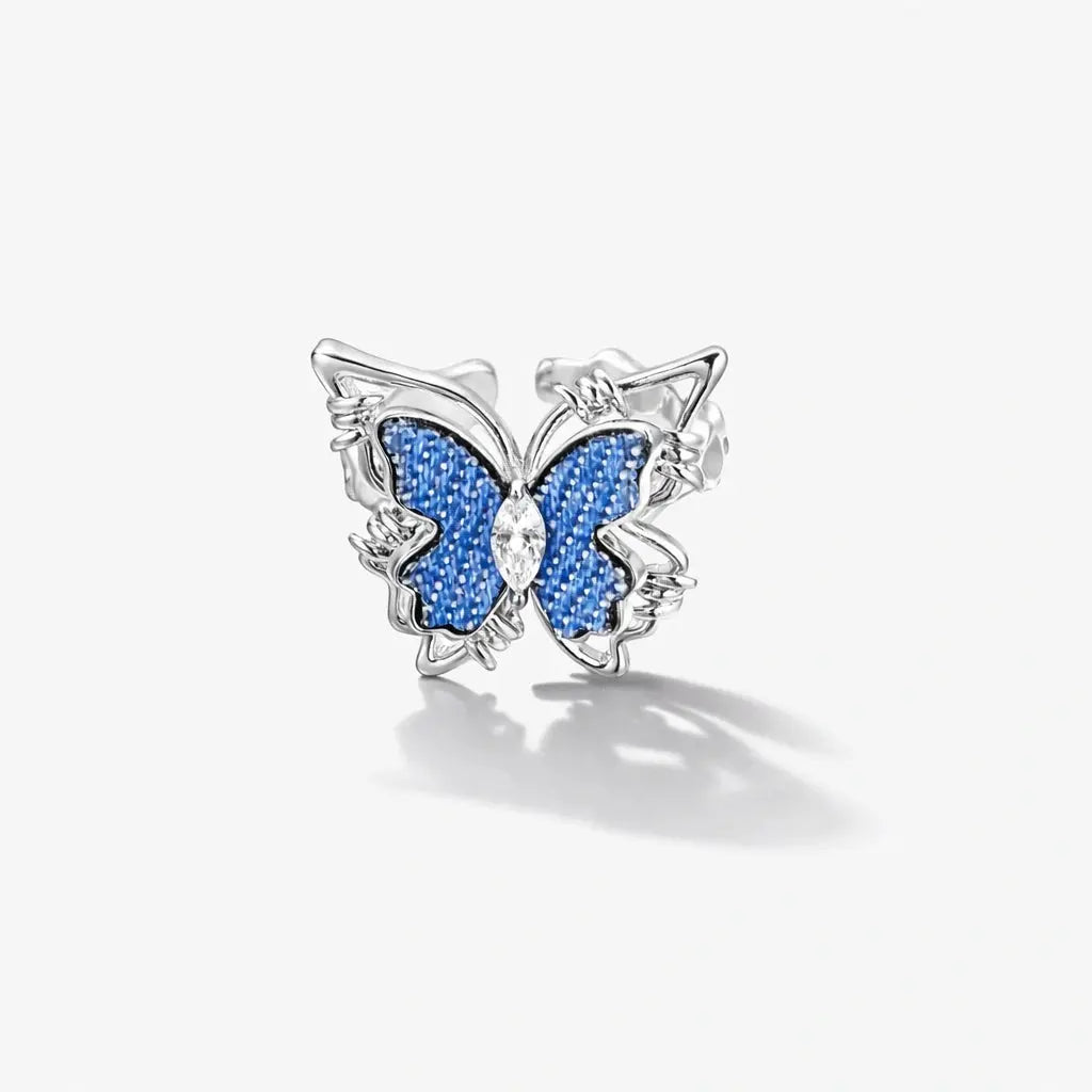 Silver butterfly stud earring with blue textured wings and clear gemstone center on white background