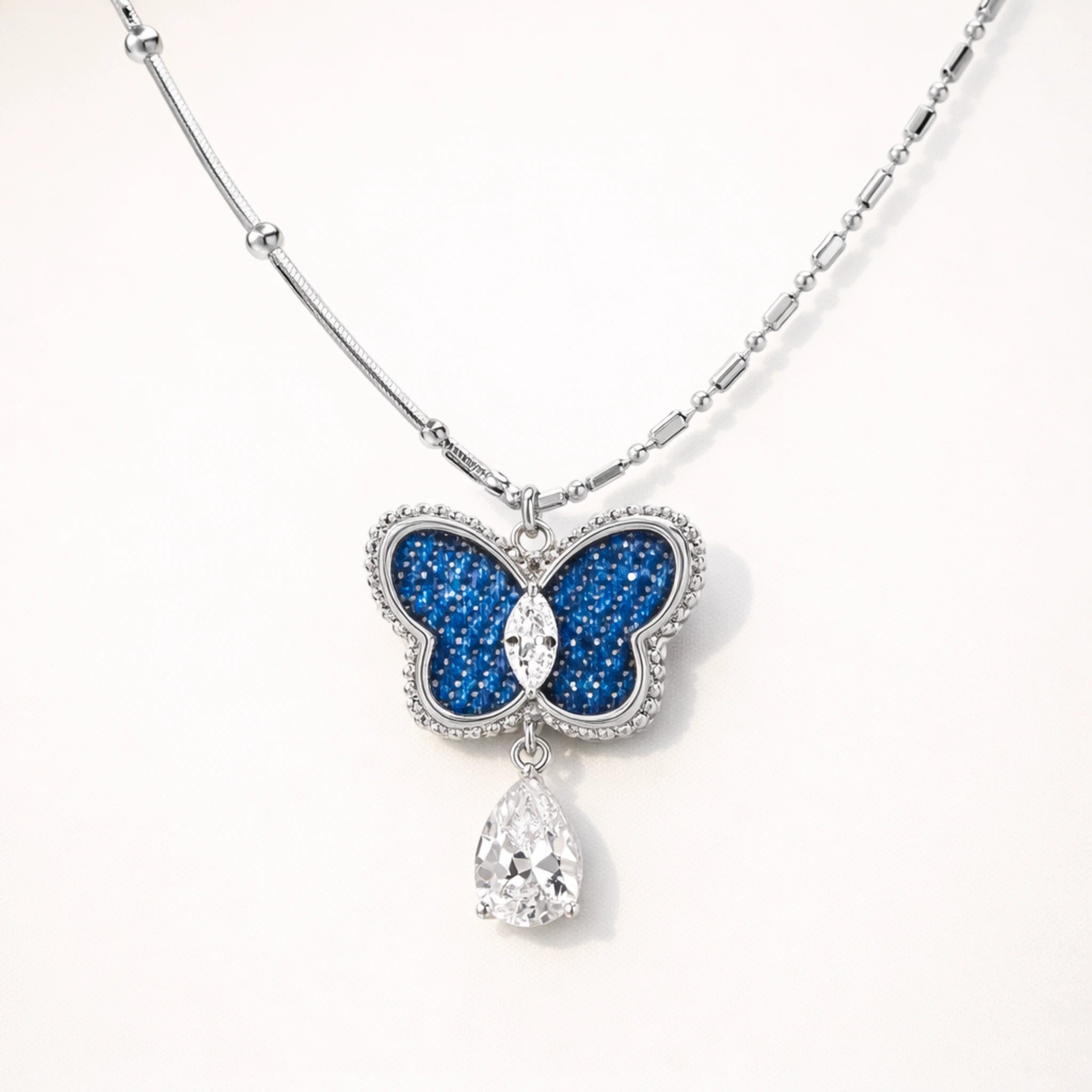 Butterfly pendant necklace with blue gem and teardrop crystal on a white background