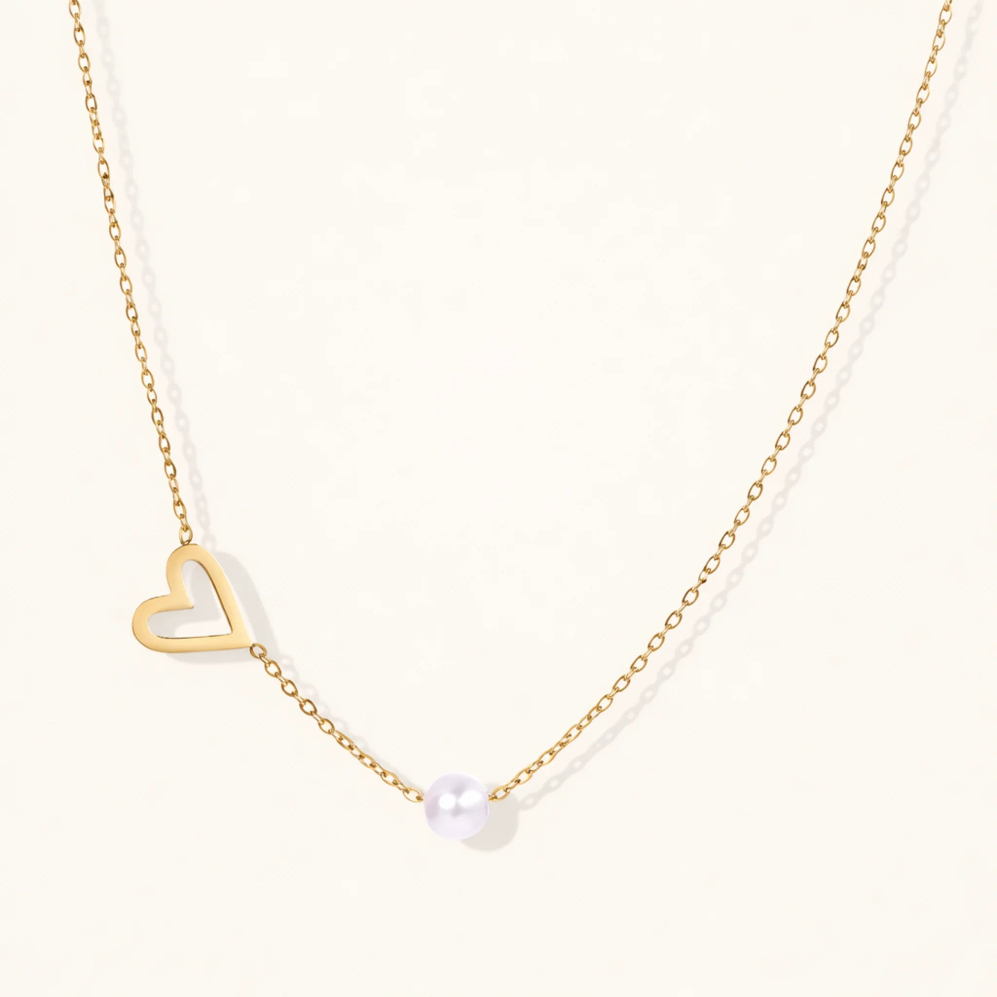 Gold necklace with a heart pendant and pearl on a white background