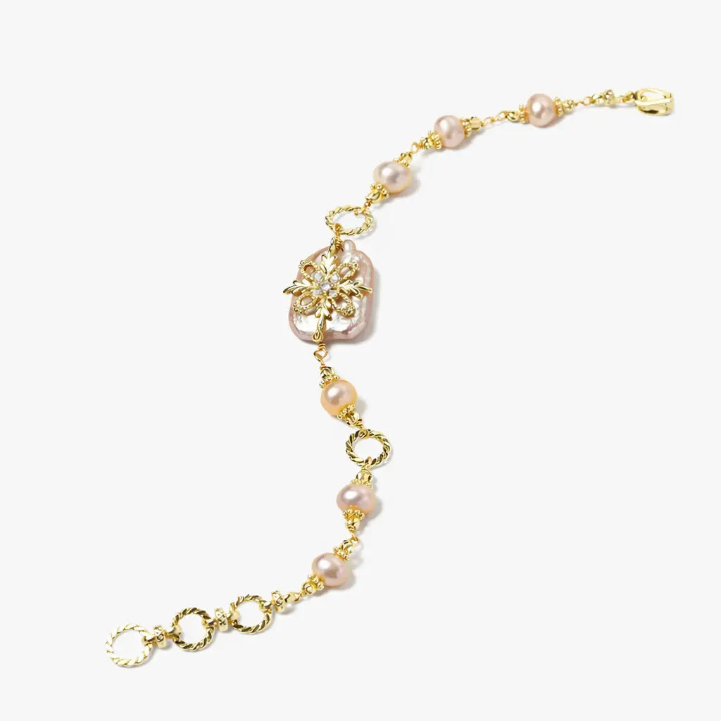 Gold bracelet with pink pearls and floral centerpiece on white background