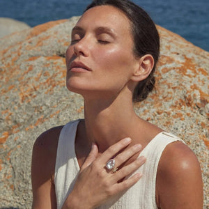 Woman with closed eyes standing on a rocky beach with ocean in the background